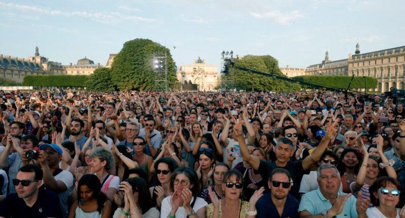 People clap as they gather to listen to music prior to the reinstallation and lift-off of the 2024 Olympic cauldron during a free concert to mark France's annual street music festival, 'Fete de la Musique', at the Jardin des Tuileries, in Paris on June 21, 2025. (Photo by GEOFFROY VAN DER HASSELT / AFP) (Photo by GEOFFROY VAN DER HASSELT/AFP via Getty Images)