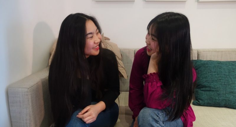 Two young women sitting on a couch, talking.
