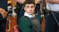 A young man wearing a bulletproof vest sits in a courtroom.