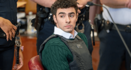 A young man wearing a bulletproof vest sits in a courtroom.