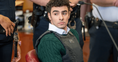 A young man wearing a bulletproof vest sits in a courtroom.