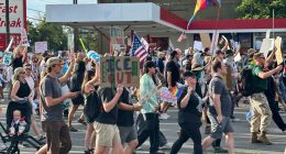 Protestors march carrying signs.