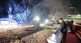 Kim Jong Un waves to a large crowd at a nighttime ceremony with fireworks.