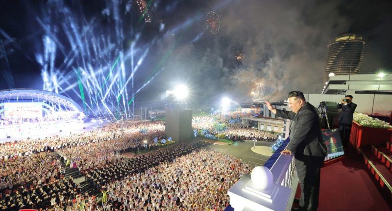 Kim Jong Un waves to a large crowd at a nighttime ceremony with fireworks.