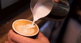 Close-up shot of a barista adding steamed milk to coffee.