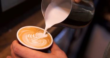 Close-up shot of a barista adding steamed milk to coffee.
