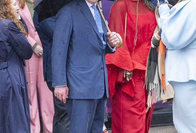 King Charles attempted to keep himself dry in the typical British wet weather by holding up a large brolly as he strolled through the streets of Shoreditch