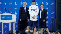 Los Angeles Dodgers' Shohei Ohtani, center, poses for a photo with owner and chairman Mark Walter, left, and president of baseball operations Andrew Friedman applaud during a news conference at Dodger Stadium Thursday, Dec. 14, 2023, in Los Angeles. (AP Photo/Ashley Landis)