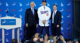 Los Angeles Dodgers' Shohei Ohtani, center, poses for a photo with owner and chairman Mark Walter, left, and president of baseball operations Andrew Friedman applaud during a news conference at Dodger Stadium Thursday, Dec. 14, 2023, in Los Angeles. (AP Photo/Ashley Landis)