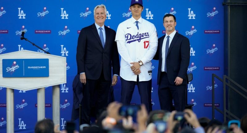 Los Angeles Dodgers' Shohei Ohtani, center, poses for a photo with owner and chairman Mark Walter, left, and president of baseball operations Andrew Friedman applaud during a news conference at Dodger Stadium Thursday, Dec. 14, 2023, in Los Angeles. (AP Photo/Ashley Landis)