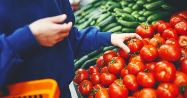 Woman in blue sweatshirt selecting tomatoes at a market.