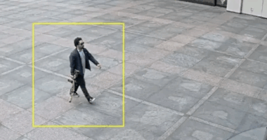 Man walking on a plaza carrying a long object.