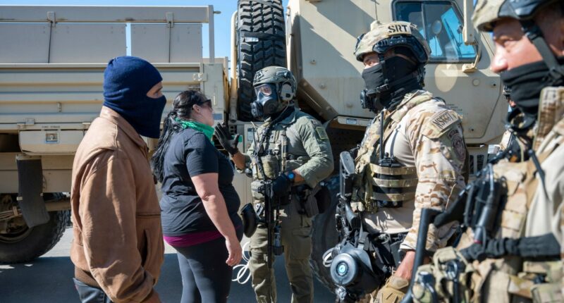Federal immigration agents talk to Rebecca Torres, second left, after she tried to block a military vehicle during a raid in the agriculture area of Camarillo, Calif., Thursday, July 10, 2025. (AP Photo/Michael Owen Baker)