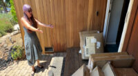Woman standing in front of her house, surrounded by numerous Amazon packages.
