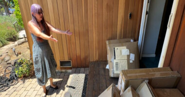 Woman standing in front of her house, surrounded by numerous Amazon packages.