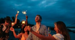Group of friends celebrating with sparklers and drinks at night.