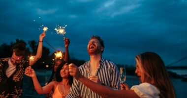 Group of friends celebrating with sparklers and drinks at night.