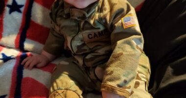 Baby in camouflage outfit on American flag blanket.