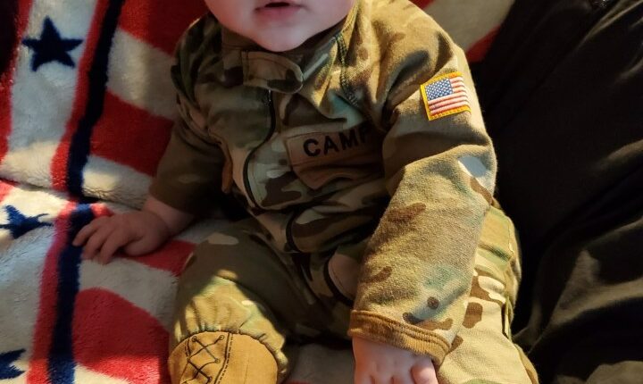 Baby in camouflage outfit on American flag blanket.