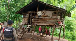 Police officers at a dilapidated wooden house in a wooded area.