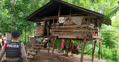 Police officers at a dilapidated wooden house in a wooded area.