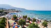 Beach scene with many people swimming and sunbathing under umbrellas.