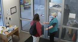 Two people wearing masks greet each other at a doorway.