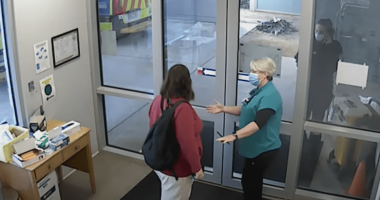 Two people wearing masks greet each other at a doorway.