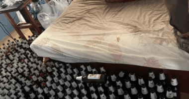 Many empty beer bottles surrounding a bed.