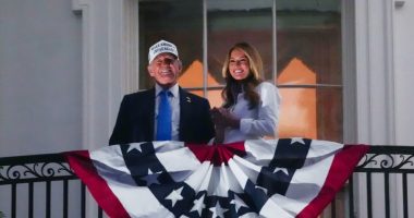 Donald and Melania Trump on a White House balcony with an American flag.