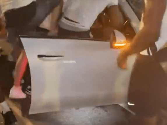 A gang surrounding a car, attacking the driver.