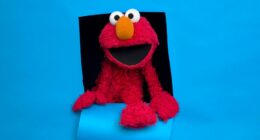 Elmo peeking through a hole in a blue background.