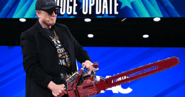 Man in a black jacket holding a red chainsaw.