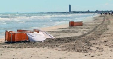Beach scene with orange barriers and a white sheet near the water.