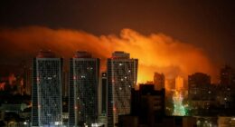Nighttime view of a city skyline illuminated by an explosion.