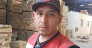 Man in a red safety vest standing in a lumberyard.