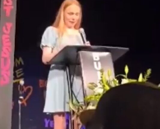Teenage girl giving a speech at a podium.