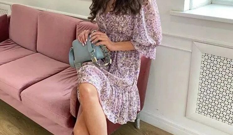 Woman in floral dress sitting on a pink couch.