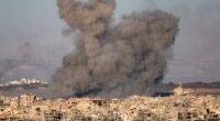 Smoke plumes rising from a bombed-out city.