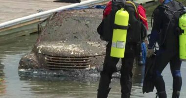 Mud-covered car pulled from water; divers nearby.
