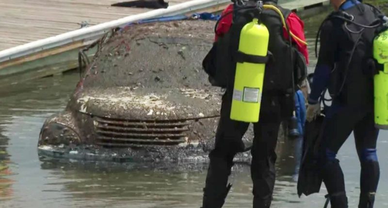 Mud-covered car pulled from water; divers nearby.