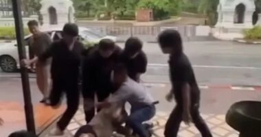 A man being restrained and kicked by several men outside a bar.