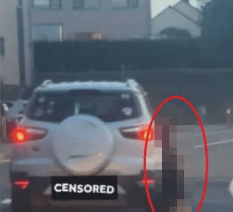 A blurred image of a person standing near the back of a car.
