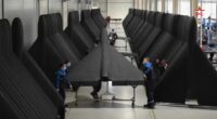 Person inspecting a large, dark-colored aircraft wing.