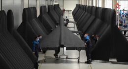 Person inspecting a large, dark-colored aircraft wing.