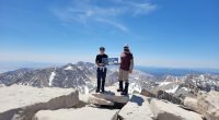 Two hikers on the summit of Mount Whitney holding a sign.