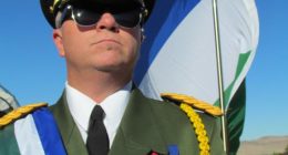 A man in a military uniform stands with a flag.