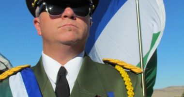 A man in a military uniform stands with a flag.