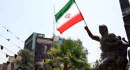 Iranian flag held aloft by a statue in Tehran, with an anti-Israel billboard in the background.