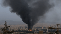 Large plume of black smoke rising over a city.